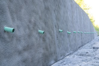 A row of green pipes protrudes from a reinforced concrete wall on a construction site, Hermann
