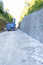 Construction site scene with blue crane next to a high concrete wall and gravel path, Hermann