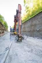 Excavator in action on a construction site next to a concrete wall with pipes, Hermann Hessebahn