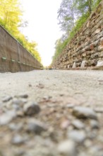 A gravel road with high walls on both sides in a wooded area, Hermann Hessebahn construction site,