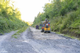 Construction machinery on a busy gravel road, surrounded by wooded slopes, Hermann Hessebahn