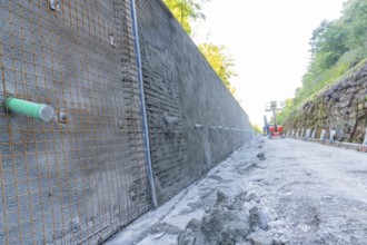 Long concrete wall with reinforcements along a construction site surrounded by trees, Hermann