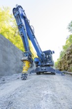 Blue crane with drill head on construction site on concrete wall, surrounded by nature, Hermann