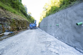 Concrete wall on construction site with blue crane, surrounded by forest and gravel path, Hermann