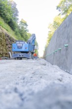 Blue excavator on a dusty road between two walls, Hermann Hessebahn construction site, Calw,