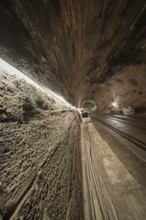 An illuminated tunnel with rails leading into the depths. The walls are made of stone and