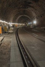 An illuminated railway tunnel, partly construction site with visible brick walls, construction of
