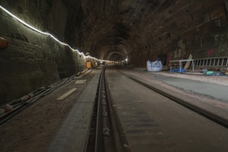 A tunnel with stone walls and railway tracks, illuminated and with building accessories,