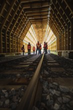 Groups of workers in a wooden railway tunnel, illuminated from the inside, construction of the