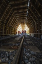 Group of employees in an illuminated wooden tunnel on railway tracks, construction of the Hermann