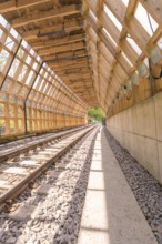Wooden tunnel structure over railway tracks, bright sunlight floods the room, construction of the