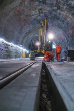 Construction workers in a tunnel carry out work with a large machine. Neon lights illuminate the