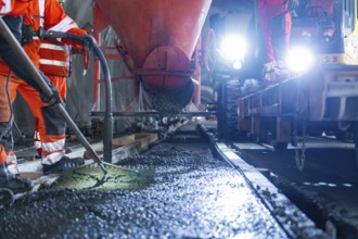 Construction workers pouring concrete under strong lighting, industrial atmosphere and safety