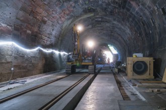 A large machine is used for construction work in the structured tunnel. Rails and wood are visible,
