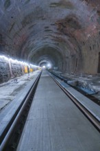 A long, illuminated tunnel with tracks and a deep perspective. The walls appear structured,