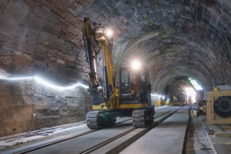 An excavator works on the rails in the illuminated tunnel. The room is structured and bright,