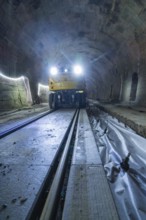 A yellow vehicle with bright lights stands in the tunnel, the rails are visible, construction of