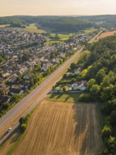 Aerial view of a village with houses, railway tracks and fields, surrounded by forest in the