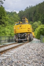 Yellow railway vehicle crossing a bridge in a wooded area, construction of the Hermann Hesse