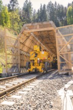 Yellow machine drives through a tunnel surrounded by wood, construction of the Hermann Hesse