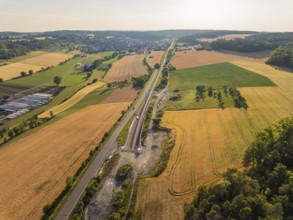 Wide landscape with fields, tracks and a long road, a village visible on the horizon under a blue
