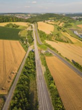 Bird's eye view of a summer landscape with fields, railway tracks and a road, surrounded by green