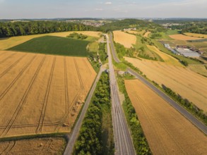 Aerial view of a summer landscape with fields, railway tracks and a road, surrounded by trees and