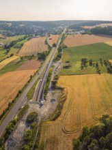 Fields and tracks, running parallel to a road, surrounded by trees, with a view of a distant