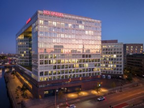 Aerial view of the Spiegel building with glass façade and illuminated offices at blue hour,