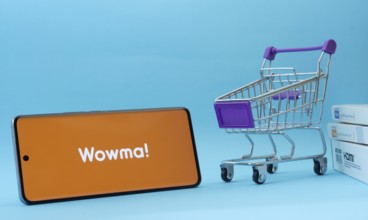 Dhaka, Bangladesh- 03 July 2025: Smartphone with wowma logo next to a small shopping cart and boxes