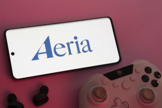 Dhaka, Bangladesh- 23 Sep 2025: Smartphone with Aeria logo, game controller, and earbuds on a pink