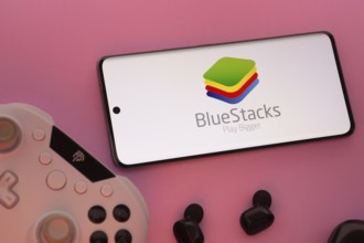 Dhaka, Bangladesh- 23 Sep 2025: Smartphone with BlueStacks logo, game controller, and earbuds on a