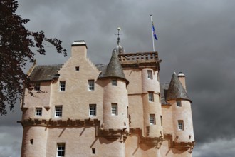 Pink castle with towers and banner in front of a threatening, cloudy sky, Craigievar Castle,