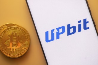 Bitcoin coin alongside smartphone displaying Upbit logo on a white screen
