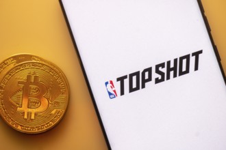 Bitcoin coin near smartphone with TopShot and NBA logos on a white screen