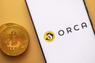 Bitcoin coin beside smartphone with Orca logo on a white screen