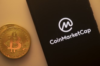 Bitcoin coin beside smartphone with CoinMarketCap logo on a black screen
