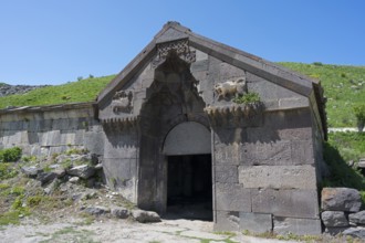 An old stone building with reliefs and a large entrance surrounded by green hills, Selim