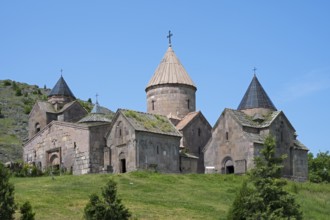 An old monastery with several towers and cross-decorated roofs on a green hill under a clear blue