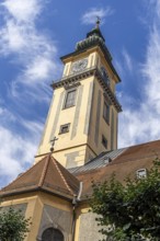 Baroque church tower with clock against a blue sky with light clouds, Old Town Linz Upper Austria
