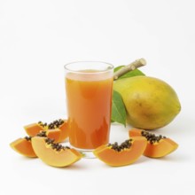 A refreshing glass of papaya juice is surrounded by fresh papaya slices and a whole papaya fruit,