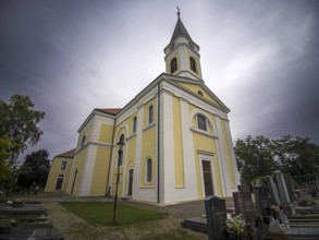 Yellow church at a cemetery with gravestones under a cloudy sky, Kammersdorf Hollabrunn Weinviertel