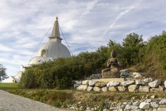 Buddha statue sitting on stones next to a pagoda in a green landscape, Stupa am Wagram Grafenwörth