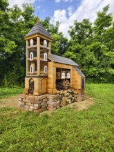 Miniature church made of wood Insect hotel surrounded by green landscape under a cloudy sky,