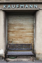 In front of a closed merchant's shop with a rusty Tor tor stands an old bench that suggests a