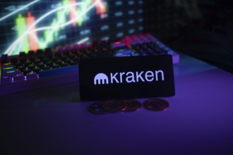 Illuminated Kraken logo on a phone with coins, trading screen in dim lighting