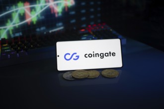 Phone with Coingate logo, set against a background of trading monitor and coins