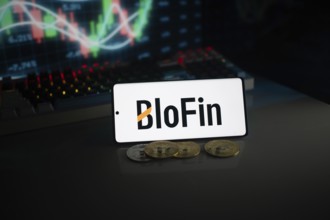 BloFin display with coins in front of an active stock chart under neon lighting