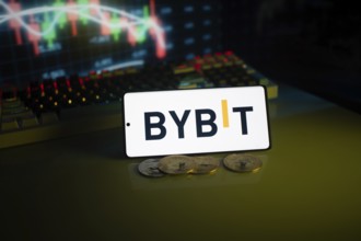 Bybit logo displayed on a phone, foregrounding trading charts and coins
