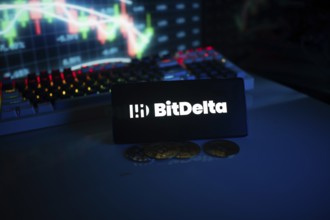 Dim-lit BitDelta logo on a phone with trading graphs and coins visible
